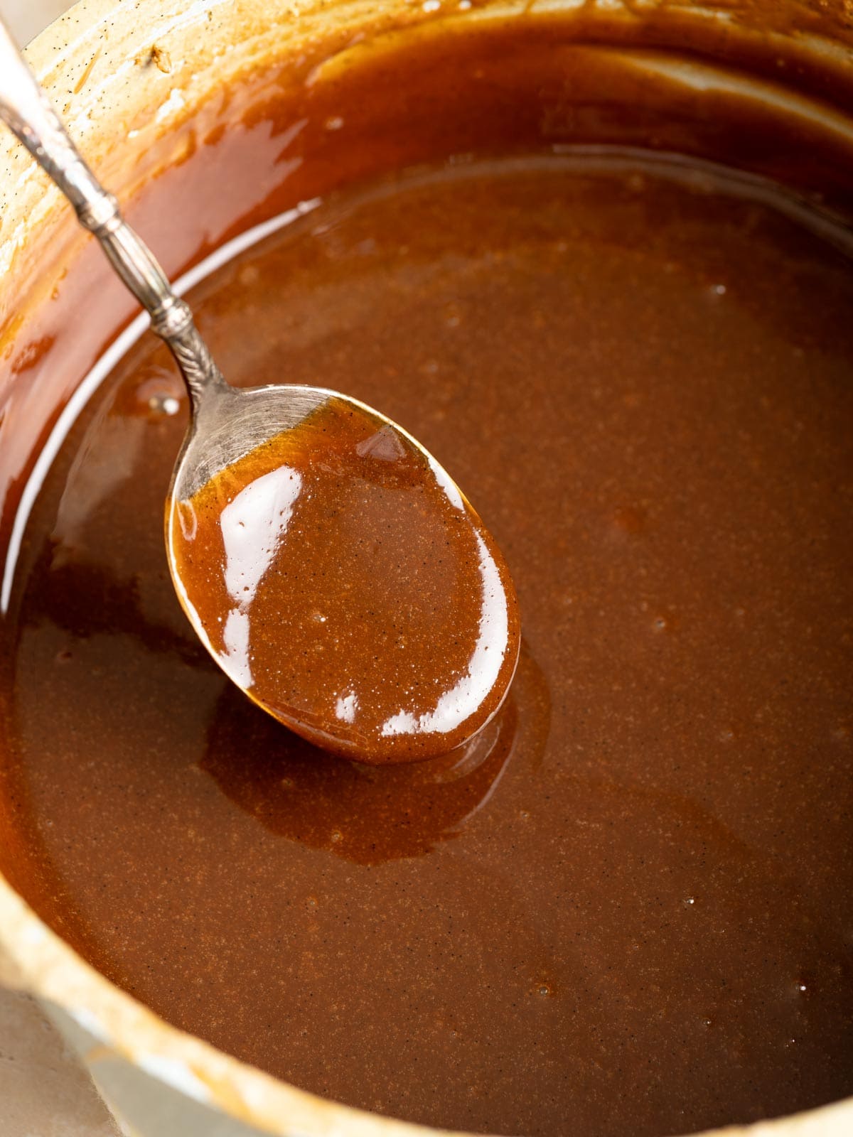 A spoon hovering over a pot of dulce de leche.