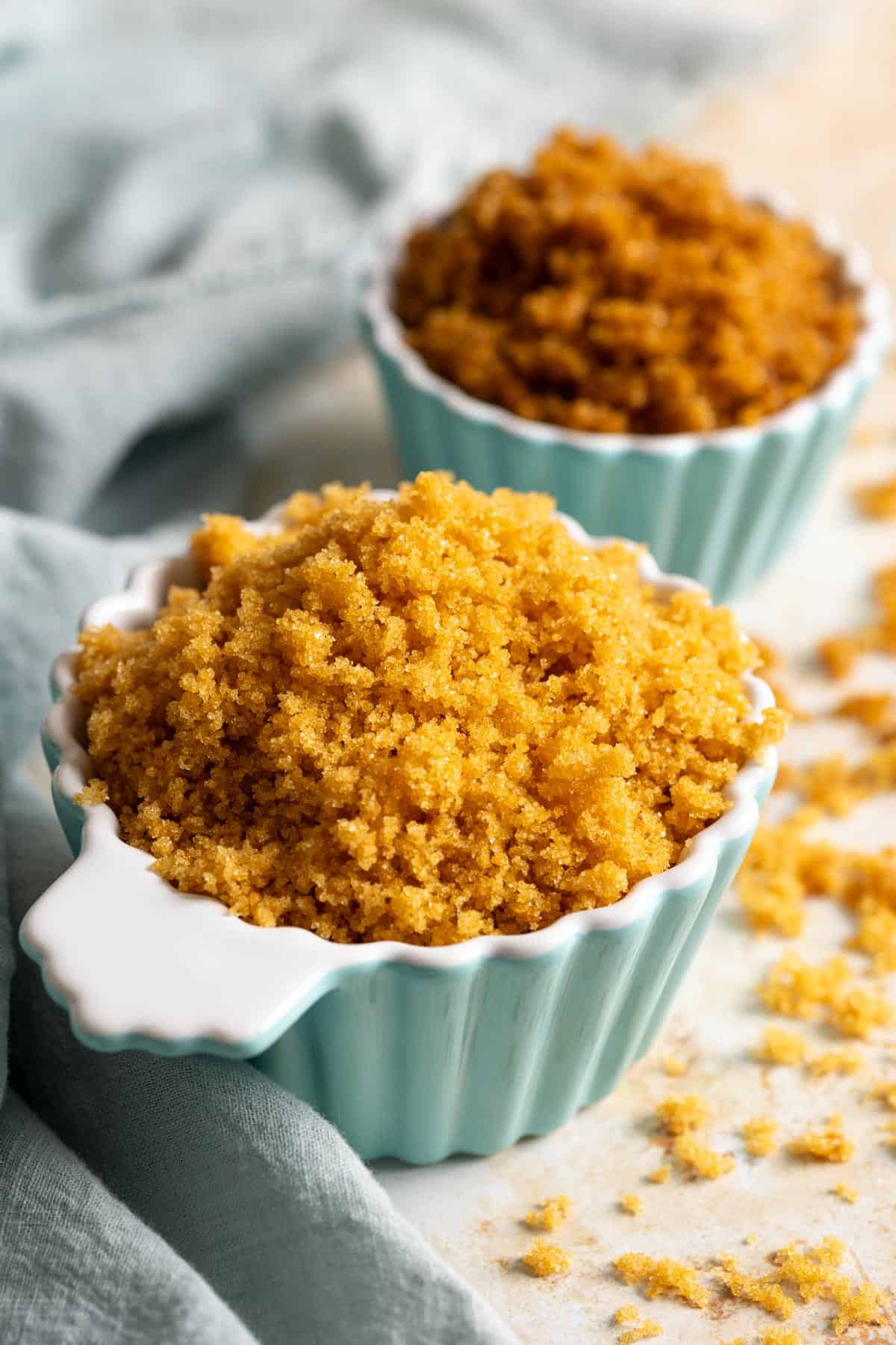 A blue cup with light brown sugar in the front and a smaller cup with dark brown sugar in the back.