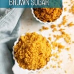 A cup of light brown sugar and a cup of dark brown sugar next to a blue tea towel.