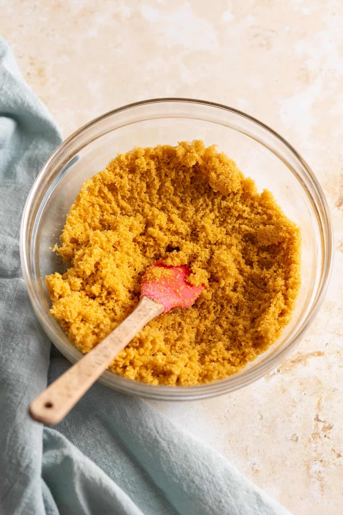 Golden brown sugar in a glass bowl with a pink spatula.