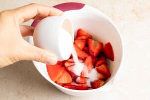 Adding sugar to sliced strawberries.