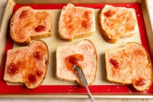 Spreading strawberry jam on sliced bread.