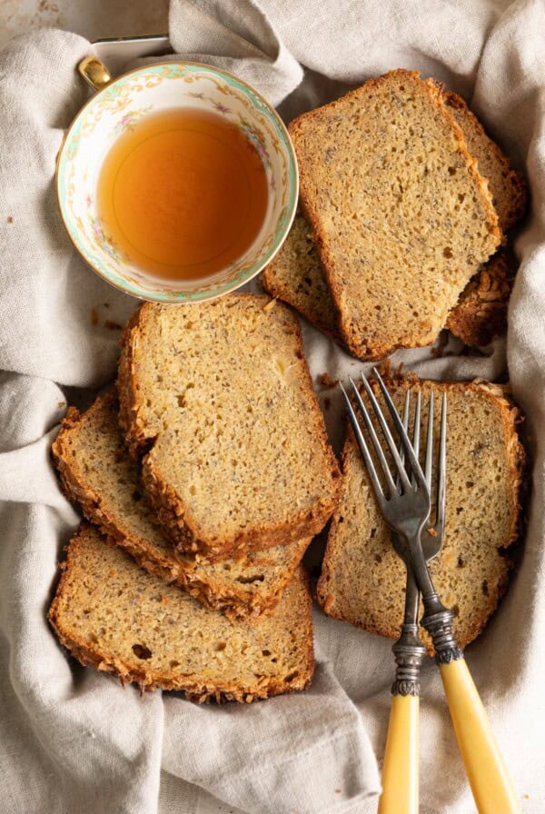 Slices of pineapple banana bread laying on top of each other next to a tea cup and 2 forks.