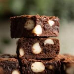 A stack of 3 chocolate brownies with large chunks of macadamia nuts.