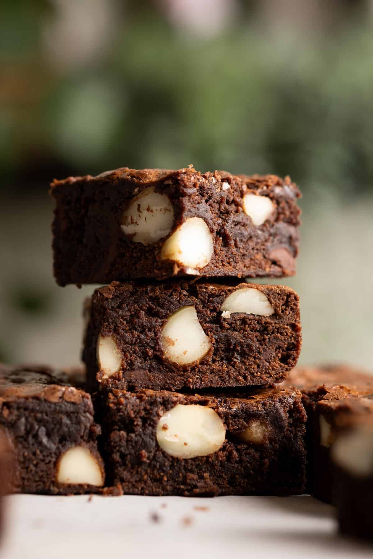 A stack of 3 chocolate brownies with large chunks of macadamia nuts.
