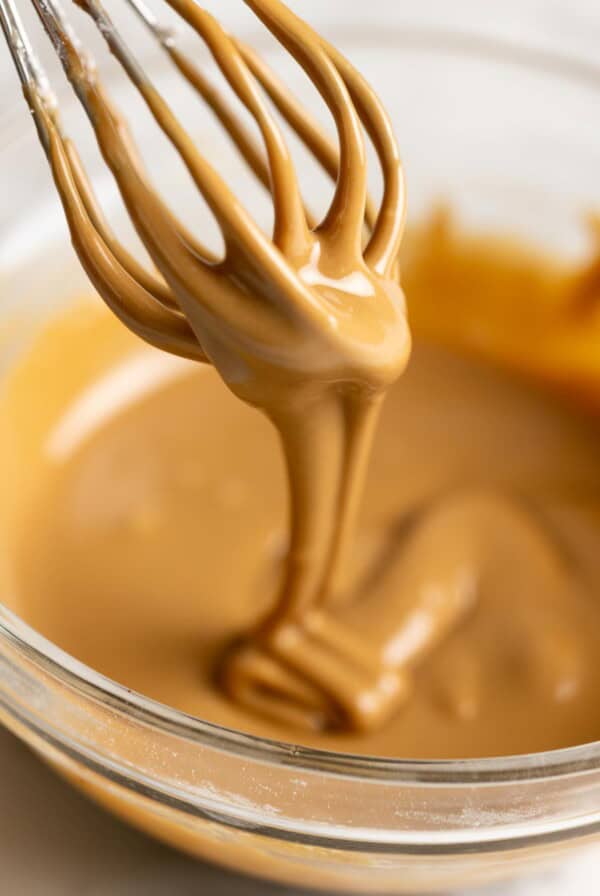 Coffee glaze is dripping back into a bowl from a whisk.